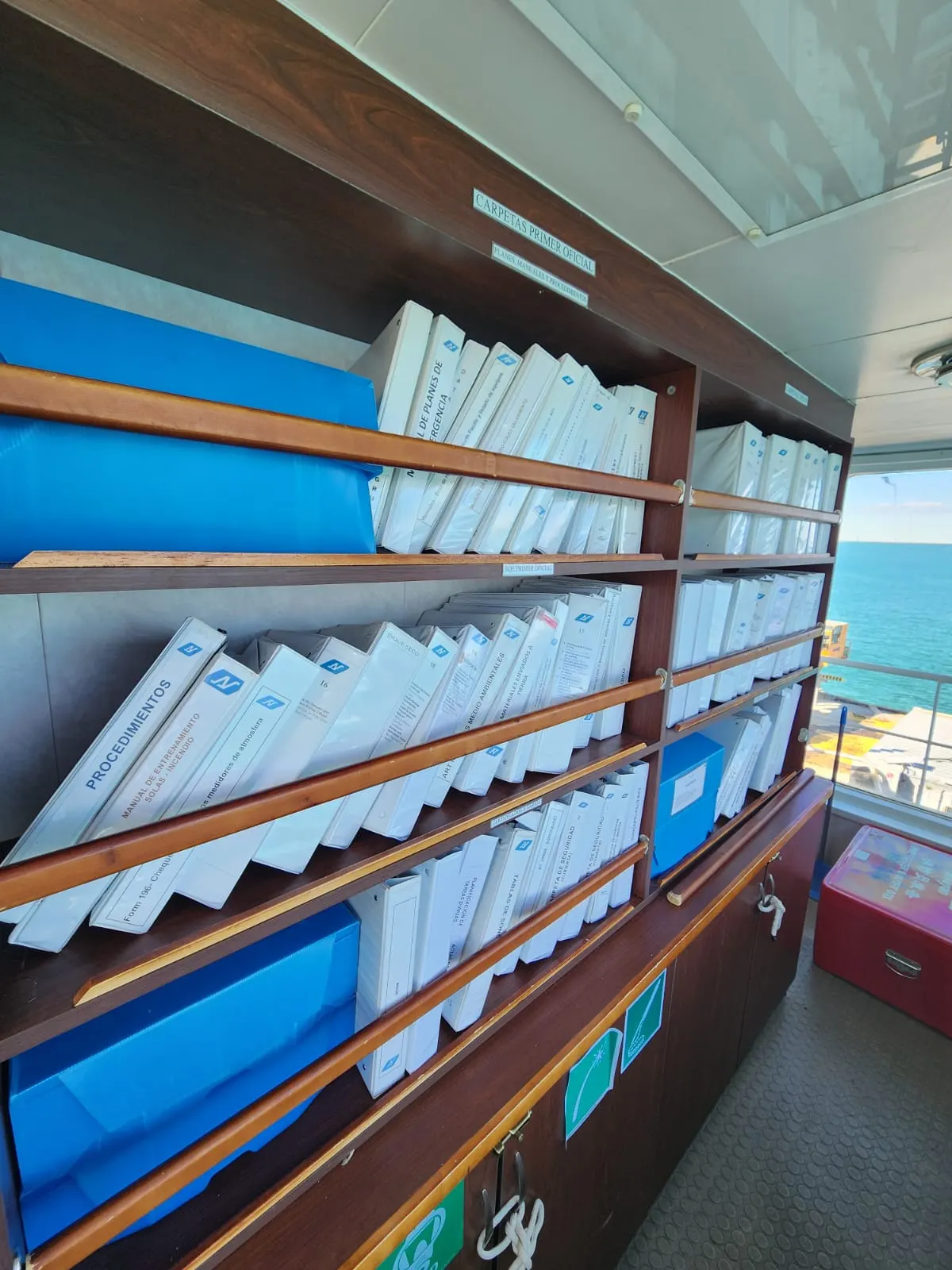 Estante con biblioratos de certificados y manuales en el puente de un buque